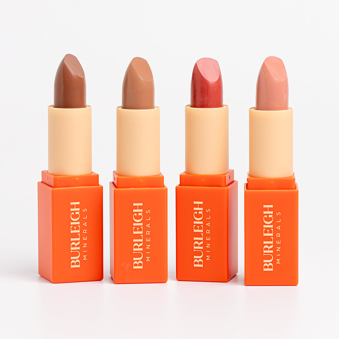 Four long wear lipsticks standing side by side with the lids off. On the left is the first shade, Chocolate Sundae, a deep brown. Second from the left is Barely There, a perfect neutral shade. Third along and second from the right is Cherry Kisses, a muted red. Finally, on the right we have the shade Pinky Nude which is a light pink.